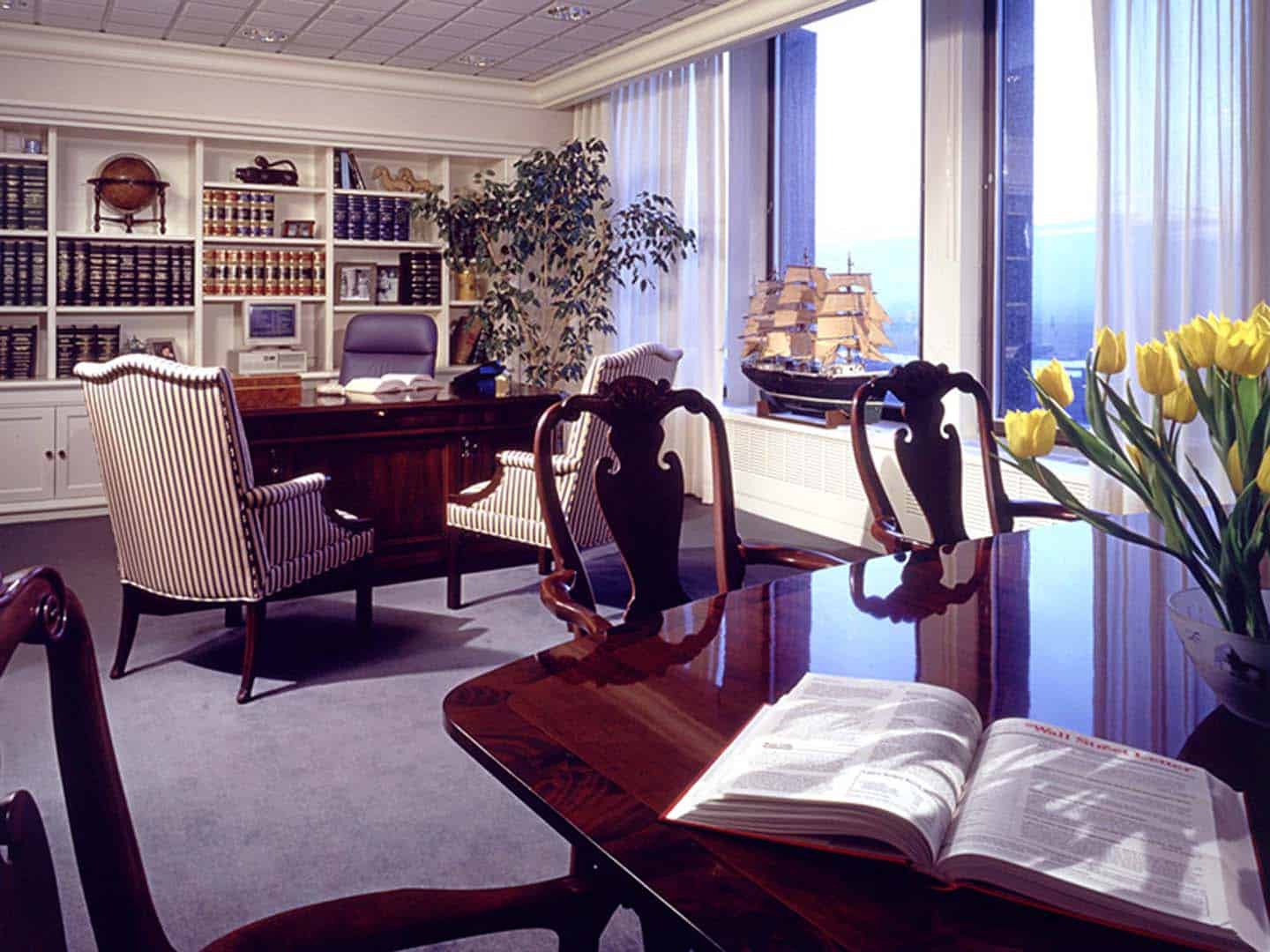 Office space with model ship, many shelves, books. and two different desk areas.