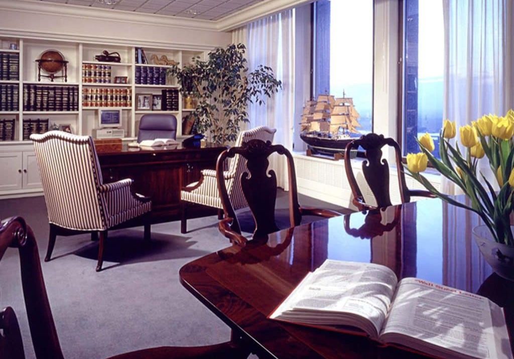 Office space with model ship, many shelves, books. and two different desk areas.