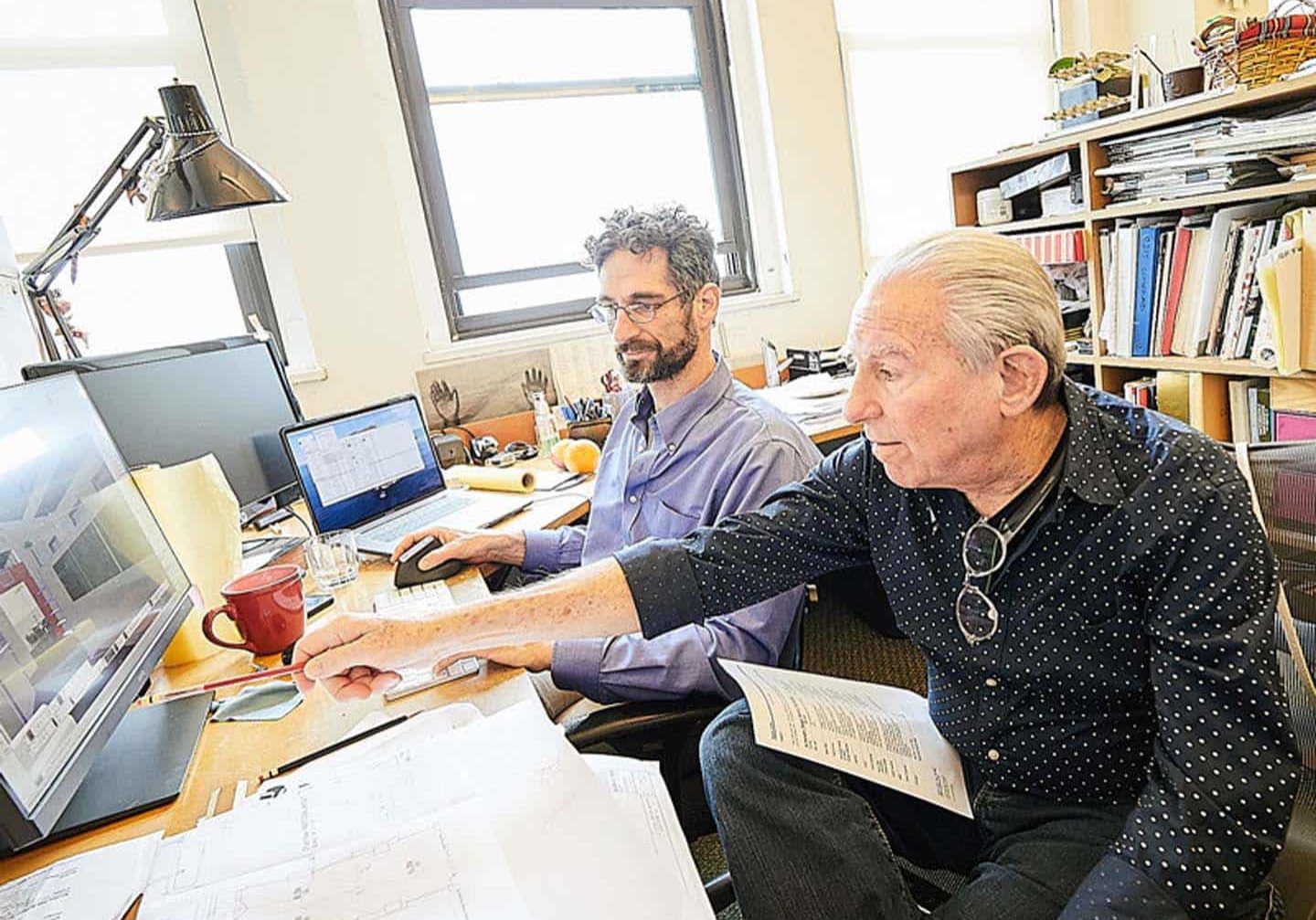 Two men in an office point at CAD mockup and give feedback
